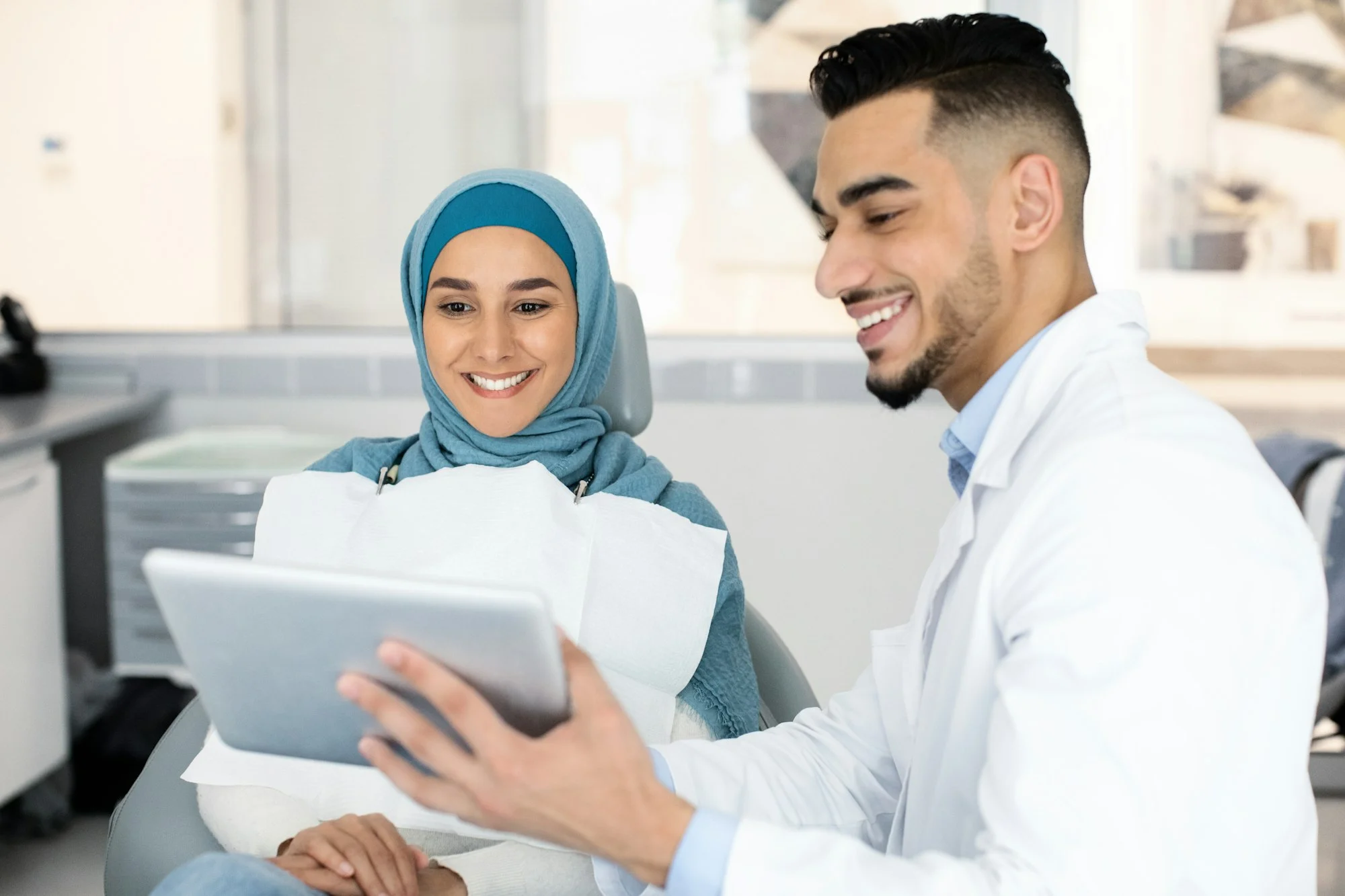 Dentist With Digital Tablet Showing Teeth Treatment Plan To Muslim Female Patient