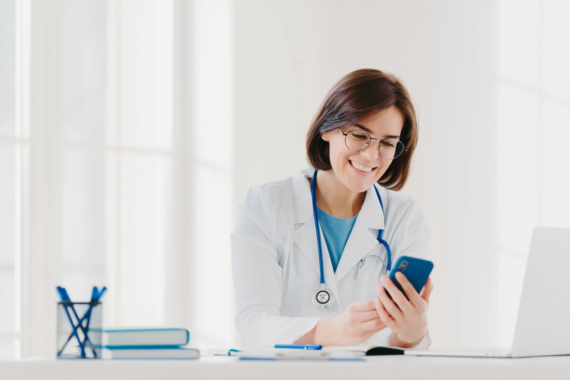 Positive female medical worker involved in chatting, holds mobile phone